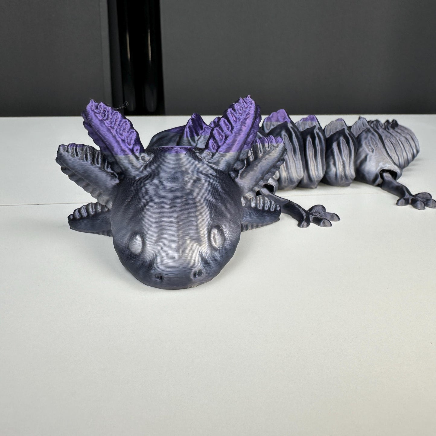 A close-up of a 3-D printed axolotl that is mostly grey and turns purple at the top